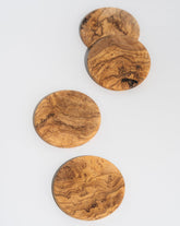A set of four round olive wood coasters with natural grain patterns.